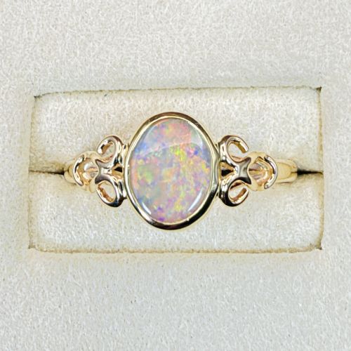 fig 1. An 18ct gold ring featuring a central oval bezel-set opal displaying colourful flash, flanked by openwork scrolled shoulders.