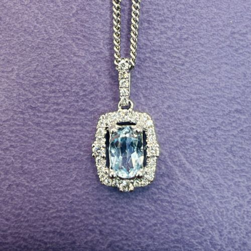 fig 1. An 18ct white gold pendant featuring a central oval-cut light blue aquamarine surrounded by a frame of round brilliant diamonds with a diamond-set bail.