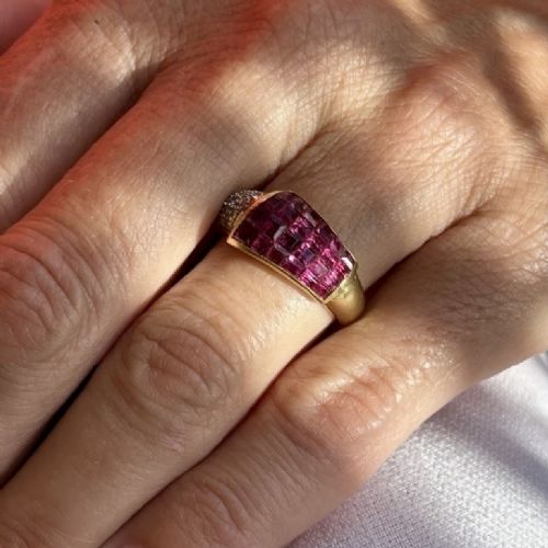 An 18ct yellow gold dress ring featuring a curved panel of princess cut red rubies alongside diamond set shoulders. View IX