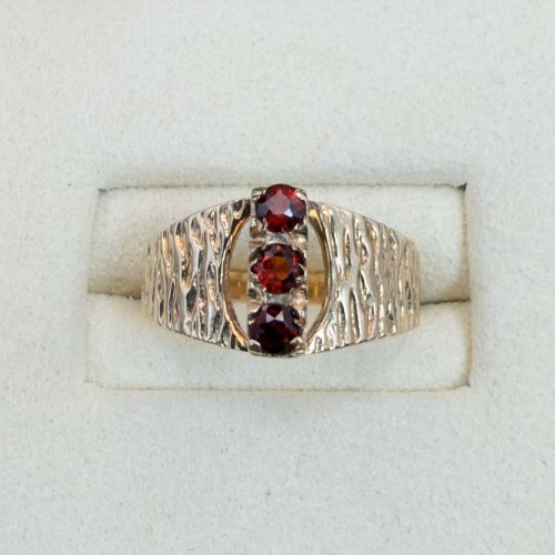 fig 1. A 1960s 9ct yellow gold ring featuring a wide band with a bark effect texture and three vertically set round-cut deep red garnets.