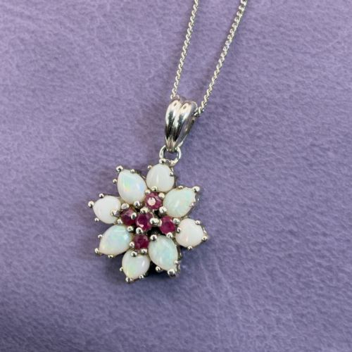 fig 1. A 9ct white gold chain and cluster pendant featuring central red rubies surrounded by pear-shaped opals in a floral design.