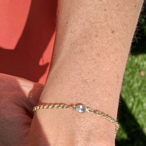 fig 1. A 9ct yellow gold rope chain bracelet featuring oval bezel-set light blue topaz gemstones at spaced intervals.