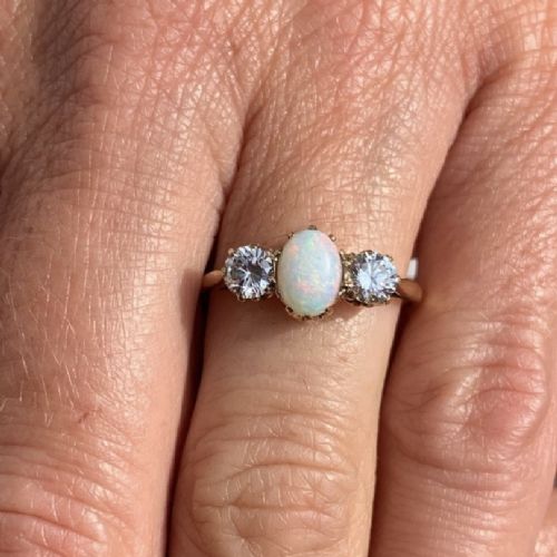 An 18ct yellow gold Art Deco ring featuring an oval cabochon opal flanked by two round diamonds in claw settings. View VI