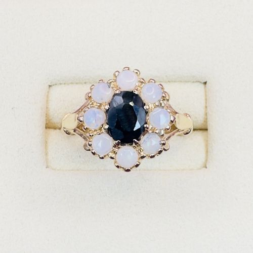 fig 1. A 14ct yellow gold cluster ring featuring a central oval dark sapphire surrounded by eight white cabochon opals in claw settings.