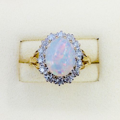 fig 1. An 18ct yellow gold ring featuring a central oval cabochon opal surrounded by a halo cluster of small round brilliant cut diamonds.