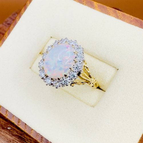 fig 2. An 18ct yellow gold ring featuring a central oval cabochon opal surrounded by a halo cluster of small round brilliant cut diamonds.