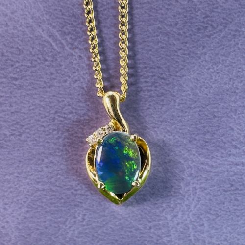 fig 1. An 18ct yellow gold necklace featuring an oval cabochon black opal displaying green and blue play-of-colour, framed in a contoured gold setting with small diamond accents.