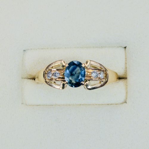 fig 1. An 18ct yellow gold ring featuring a central oval-cut blue sapphire flanked by round diamonds set into carved shoulders.