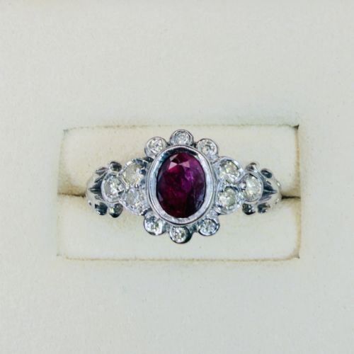 fig 1. An 18ct white gold cluster ring featuring a central oval bezel-set red ruby framed by small round diamonds and decorative shoulders.