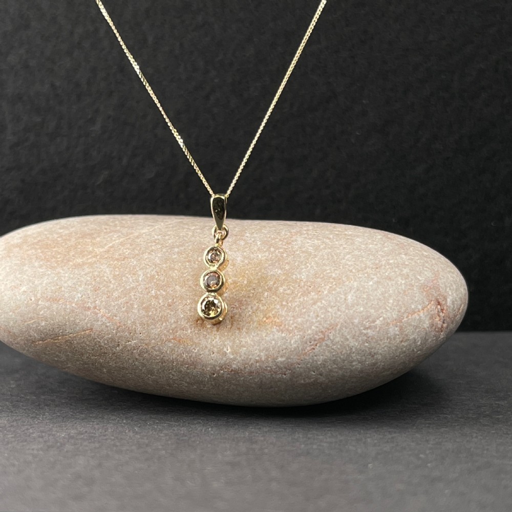 A 9ct yellow gold fine link chain necklace featuring a vertical drop pendant set with three round brilliant cut diamonds in bezel settings. View II