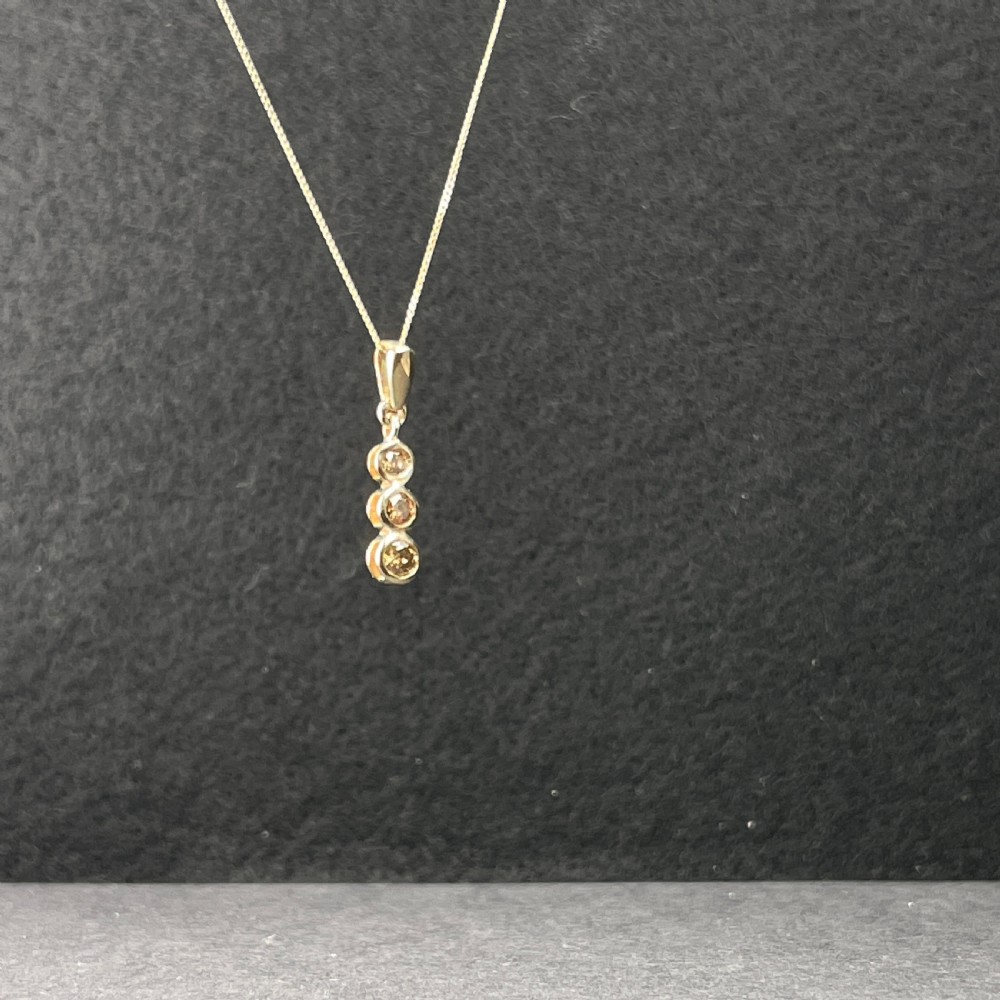 A 9ct yellow gold fine link chain necklace featuring a vertical drop pendant set with three round brilliant cut diamonds in bezel settings. View IV
