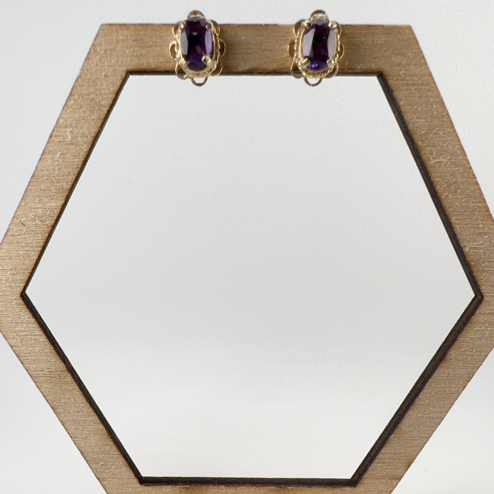 A pair of 9ct yellow gold stud earrings featuring oval cut purple amethyst gemstones surrounded by decorative scalloped filigree borders. View VII