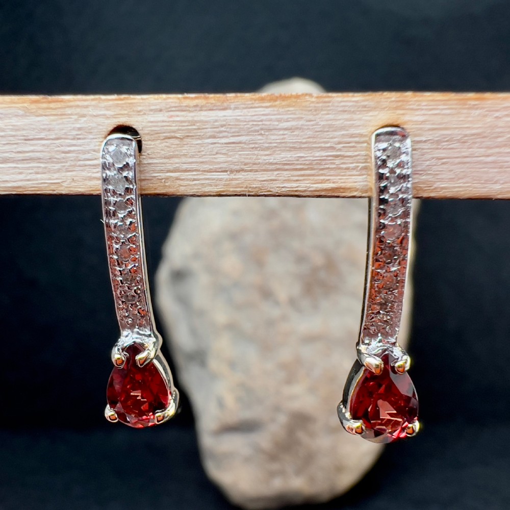 A pair of 9ct gold drop earrings featuring curved diamond-set bars terminating in pear-shaped red garnets, accompanied by gold scroll backs. View V