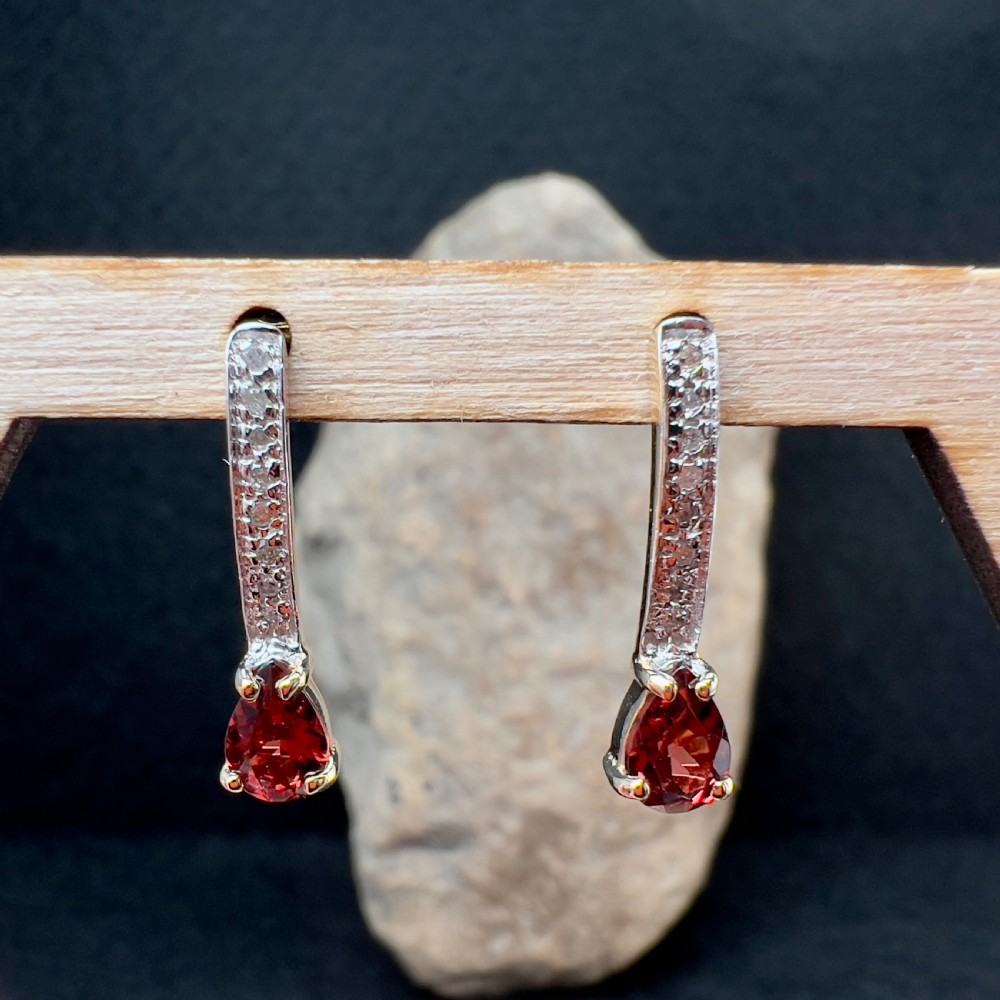 A pair of 9ct gold drop earrings featuring curved diamond-set bars terminating in pear-shaped red garnets, accompanied by gold scroll backs. View VII