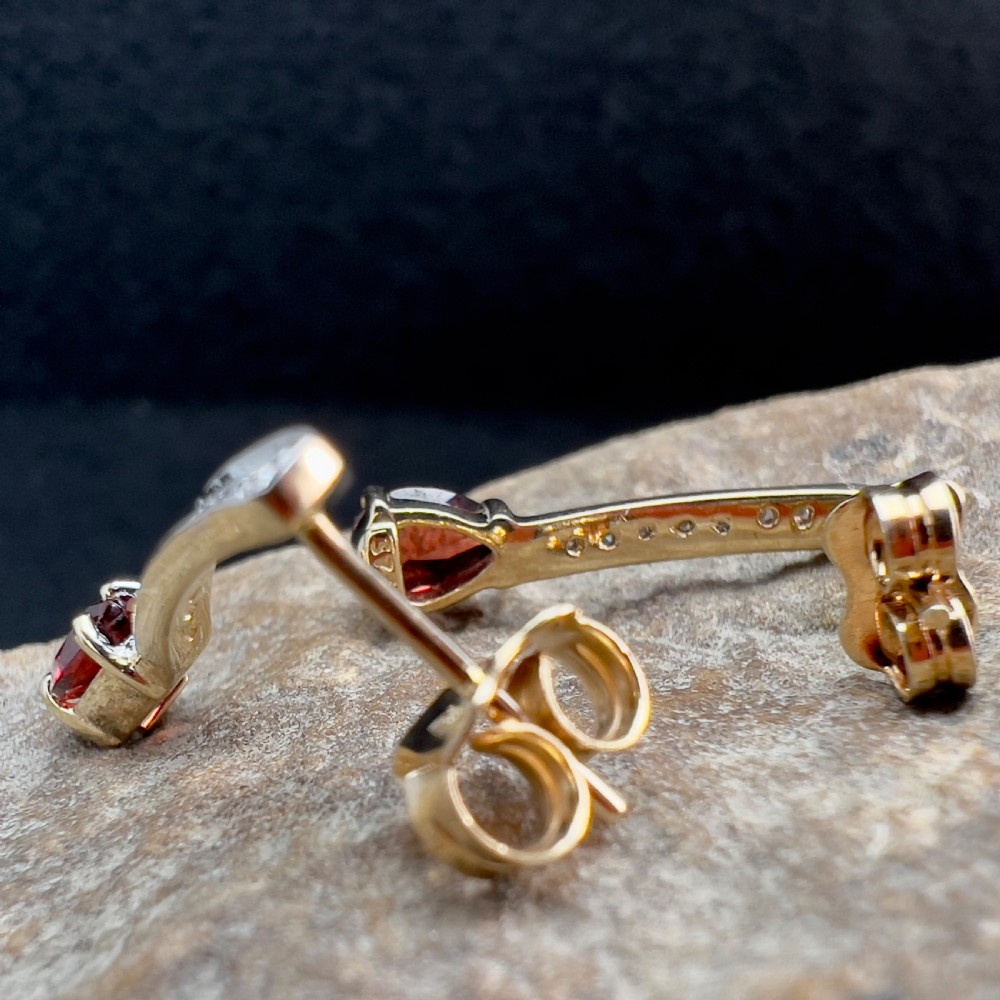 A pair of 9ct gold drop earrings featuring curved diamond-set bars terminating in pear-shaped red garnets, accompanied by gold scroll backs. View XII