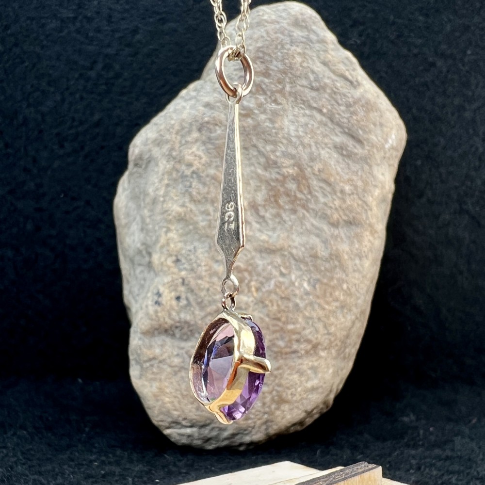 A 9ct gold pendant necklace featuring an elongated tapered bail drop suspending an oval faceted purple amethyst in a claw setting. View V
