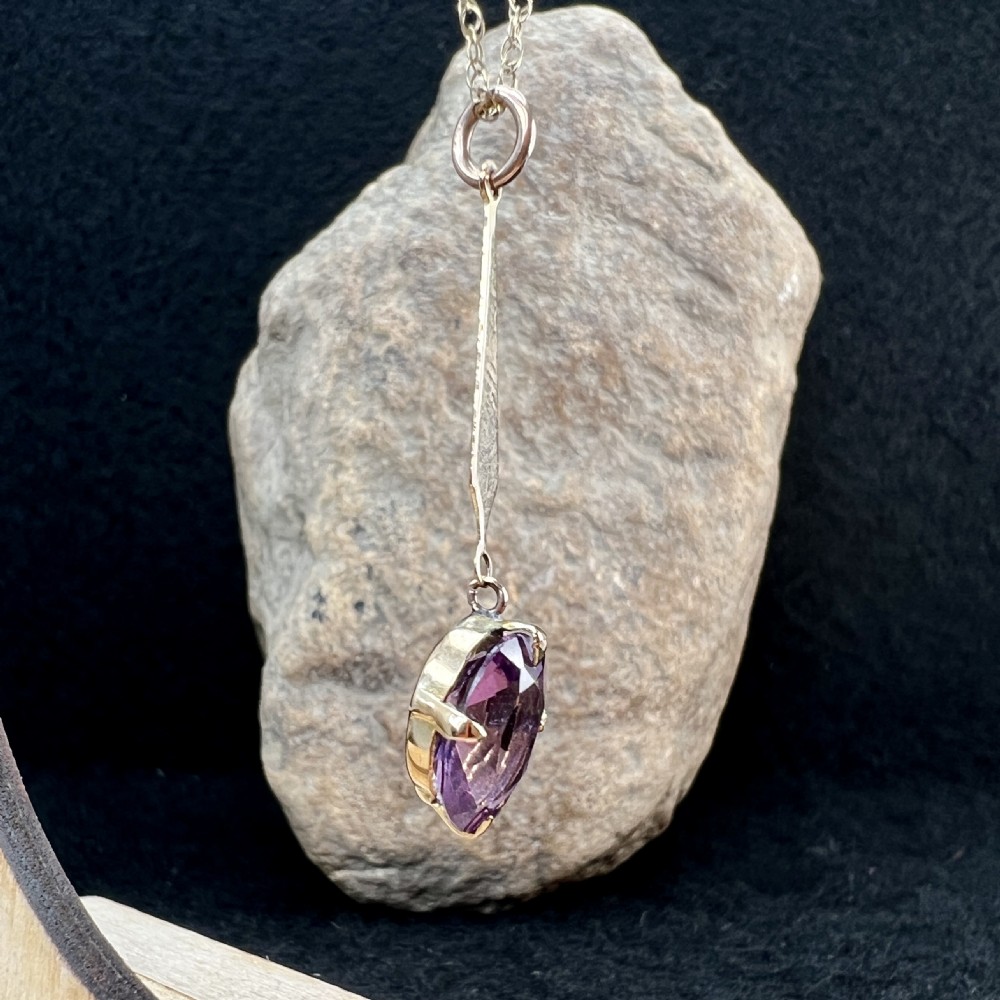 A 9ct gold pendant necklace featuring an elongated tapered bail drop suspending an oval faceted purple amethyst in a claw setting. View VII