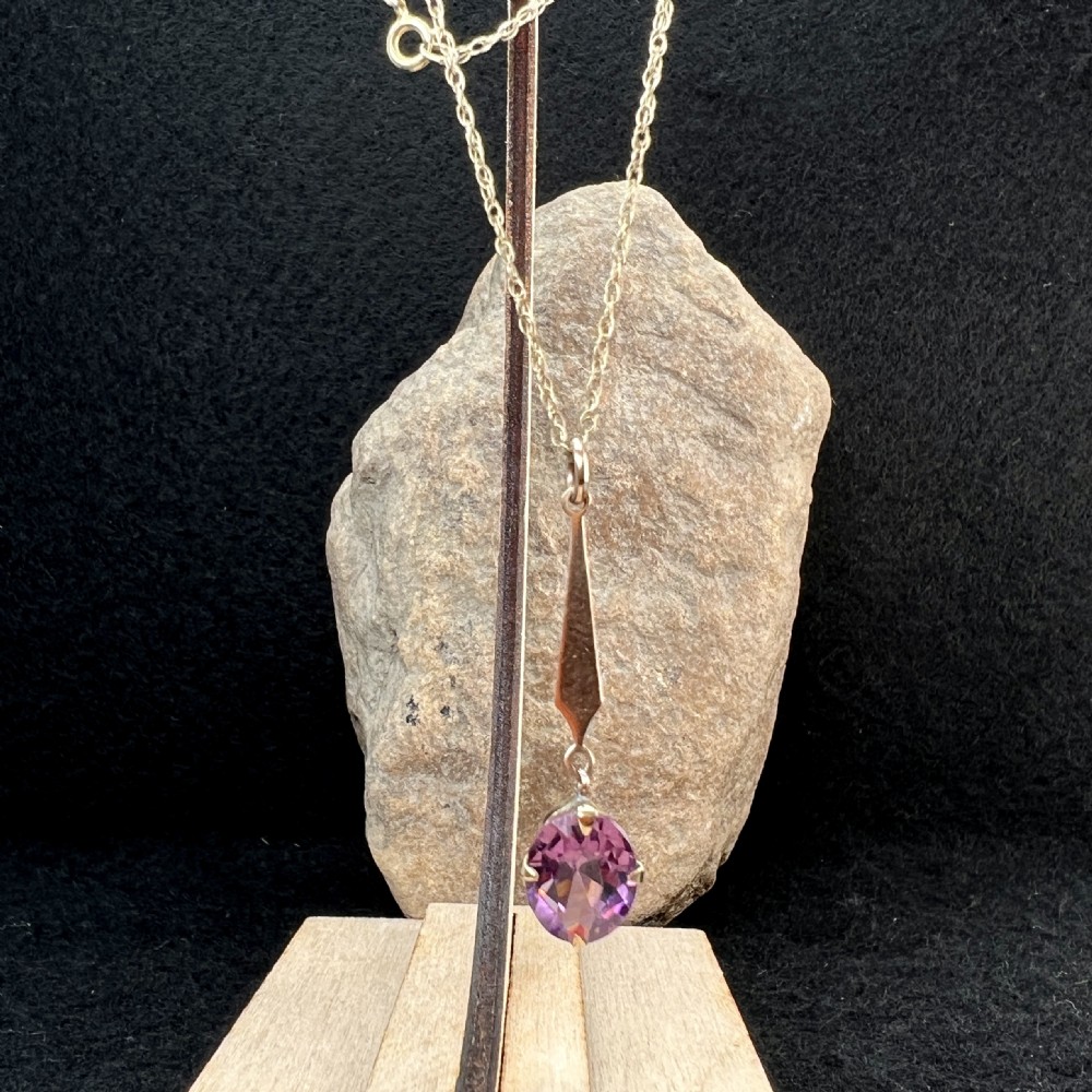 A 9ct gold pendant necklace featuring an elongated tapered bail drop suspending an oval faceted purple amethyst in a claw setting. View IX