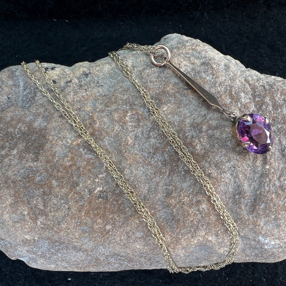 A 9ct gold pendant necklace featuring an elongated tapered bail drop suspending an oval faceted purple amethyst in a claw setting. View XI