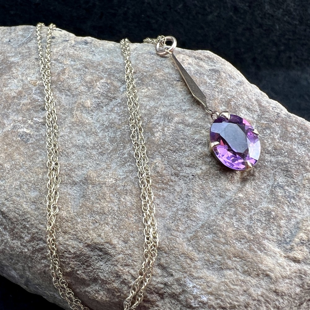 A 9ct gold pendant necklace featuring an elongated tapered bail drop suspending an oval faceted purple amethyst in a claw setting. View XIII