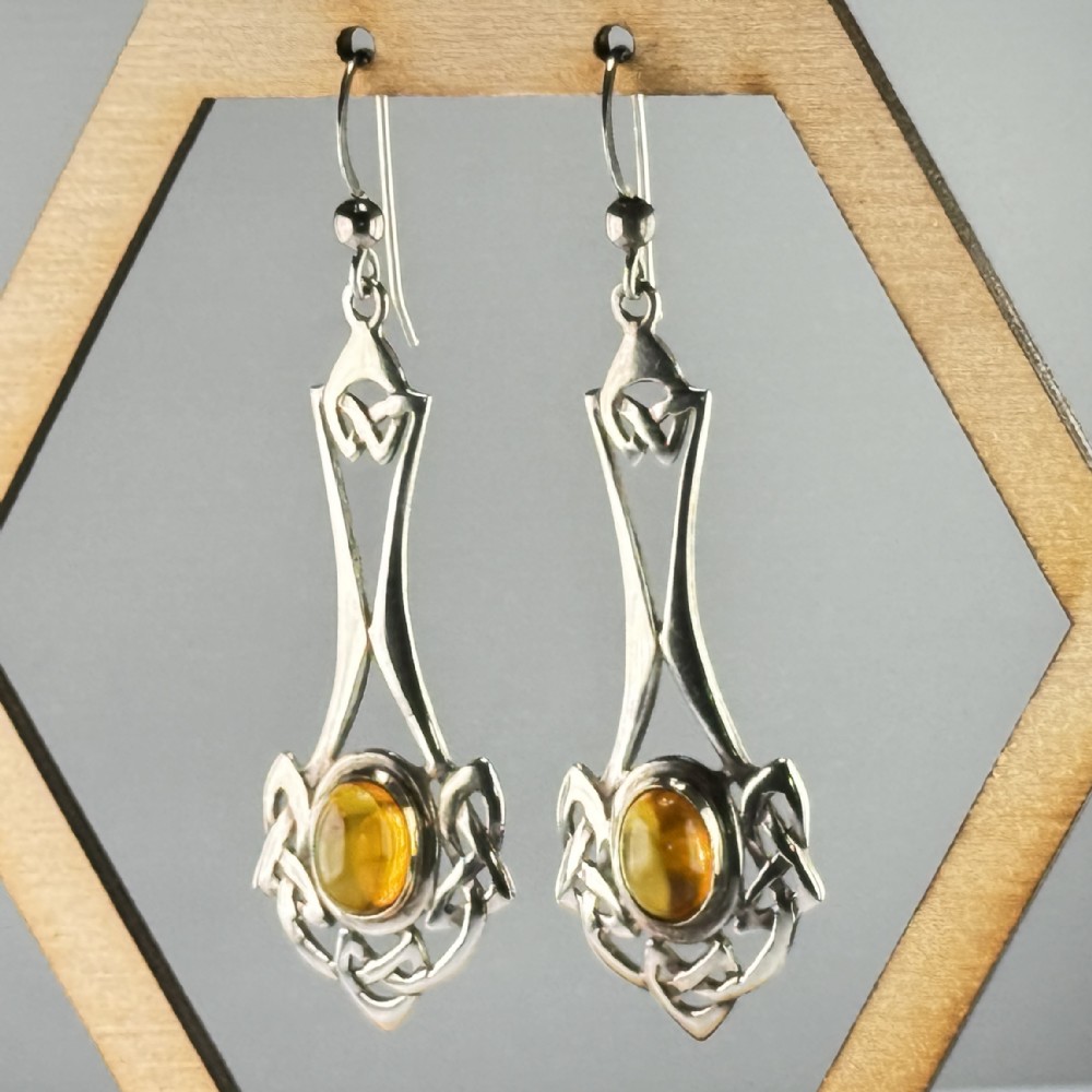 A pair of sterling silver drop earrings featuring intricate openwork Celtic knot patterns encasing oval amber cabochon stones.