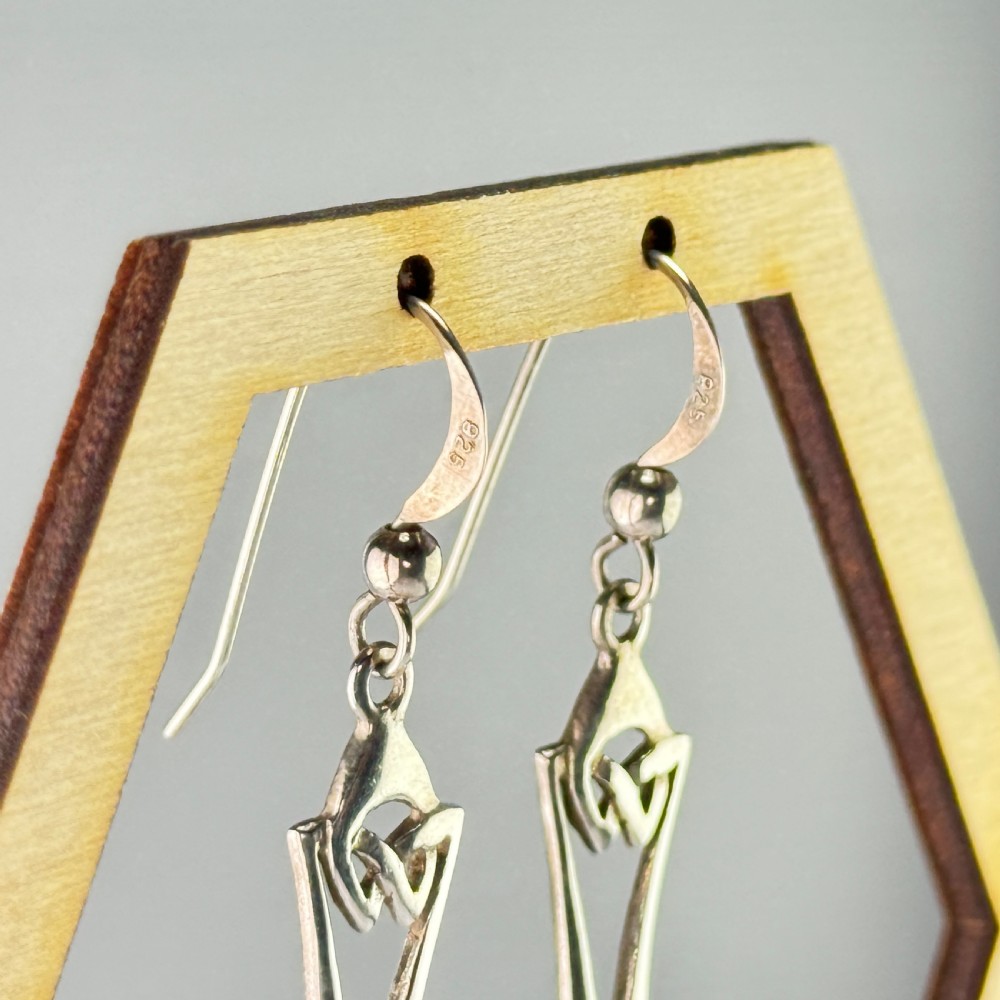 A pair of sterling silver drop earrings featuring intricate openwork Celtic knot patterns encasing oval amber cabochon stones. View VI