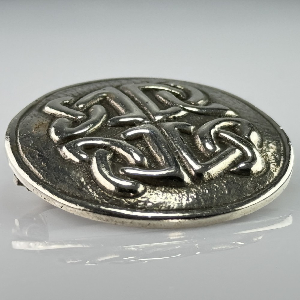 A circular silver brooch featuring raised Celtic knotwork patterns against a textured oxidised background. View II