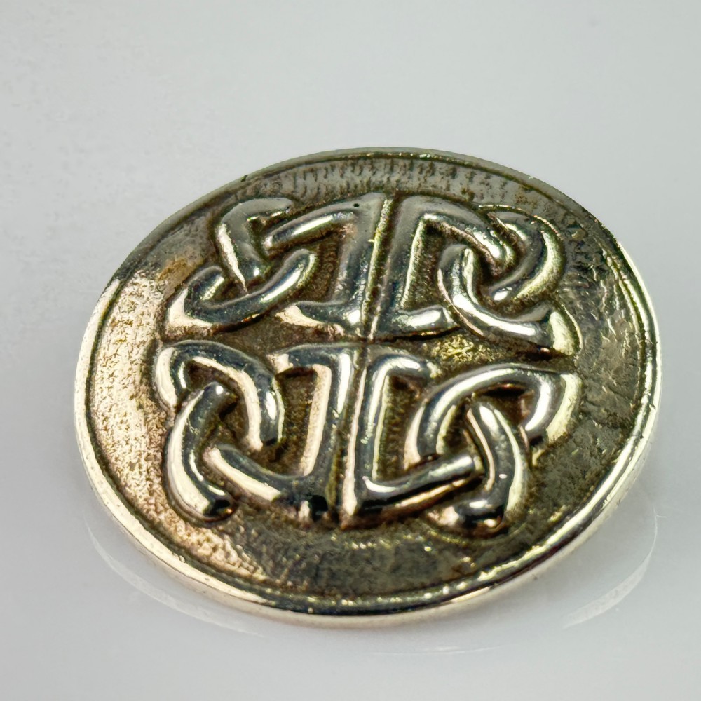 A circular silver brooch featuring raised Celtic knotwork patterns against a textured oxidised background. View IV