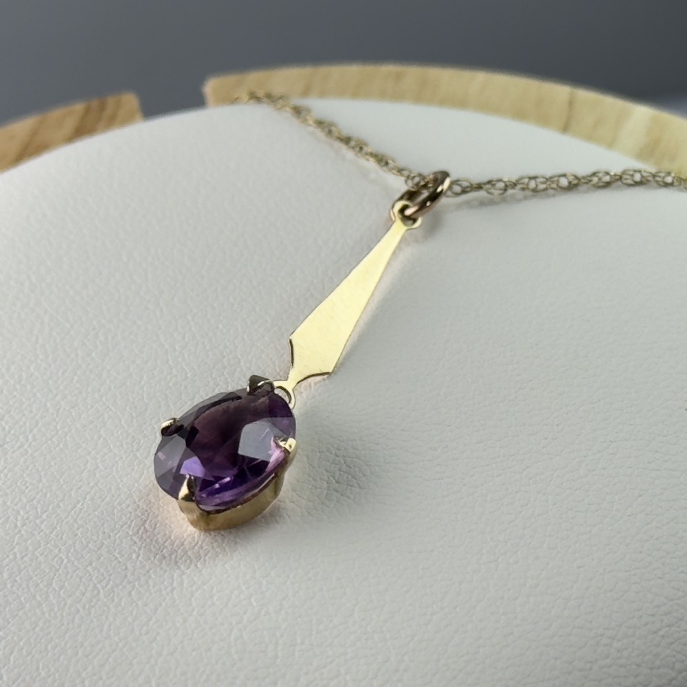 A 9ct gold pendant necklace featuring an elongated tapered bail drop suspending an oval faceted purple amethyst in a claw setting. View IV