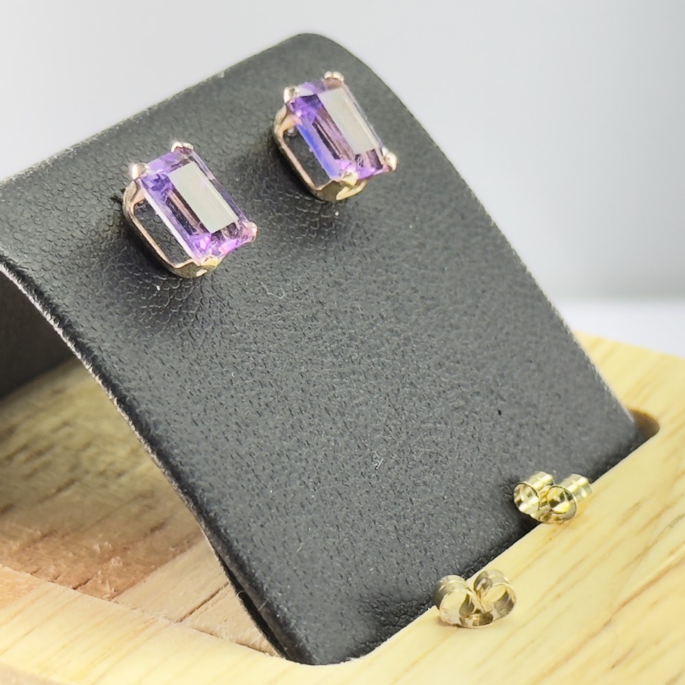 A pair of 9ct gold stud earrings mounted with rectangular emerald-cut purple amethyst gemstones and matching scroll backs.