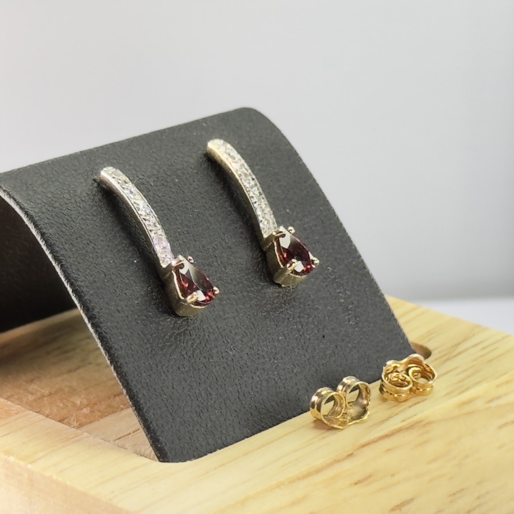 A pair of 9ct gold drop earrings featuring curved diamond-set bars terminating in pear-shaped red garnets, accompanied by gold scroll backs.