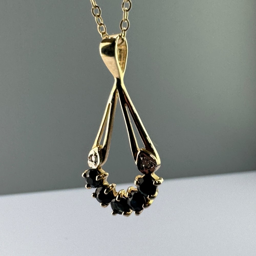 A 9ct yellow gold openwork drop pendant set with five round dark blue sapphires and two small accent diamonds on a fine chain. View II