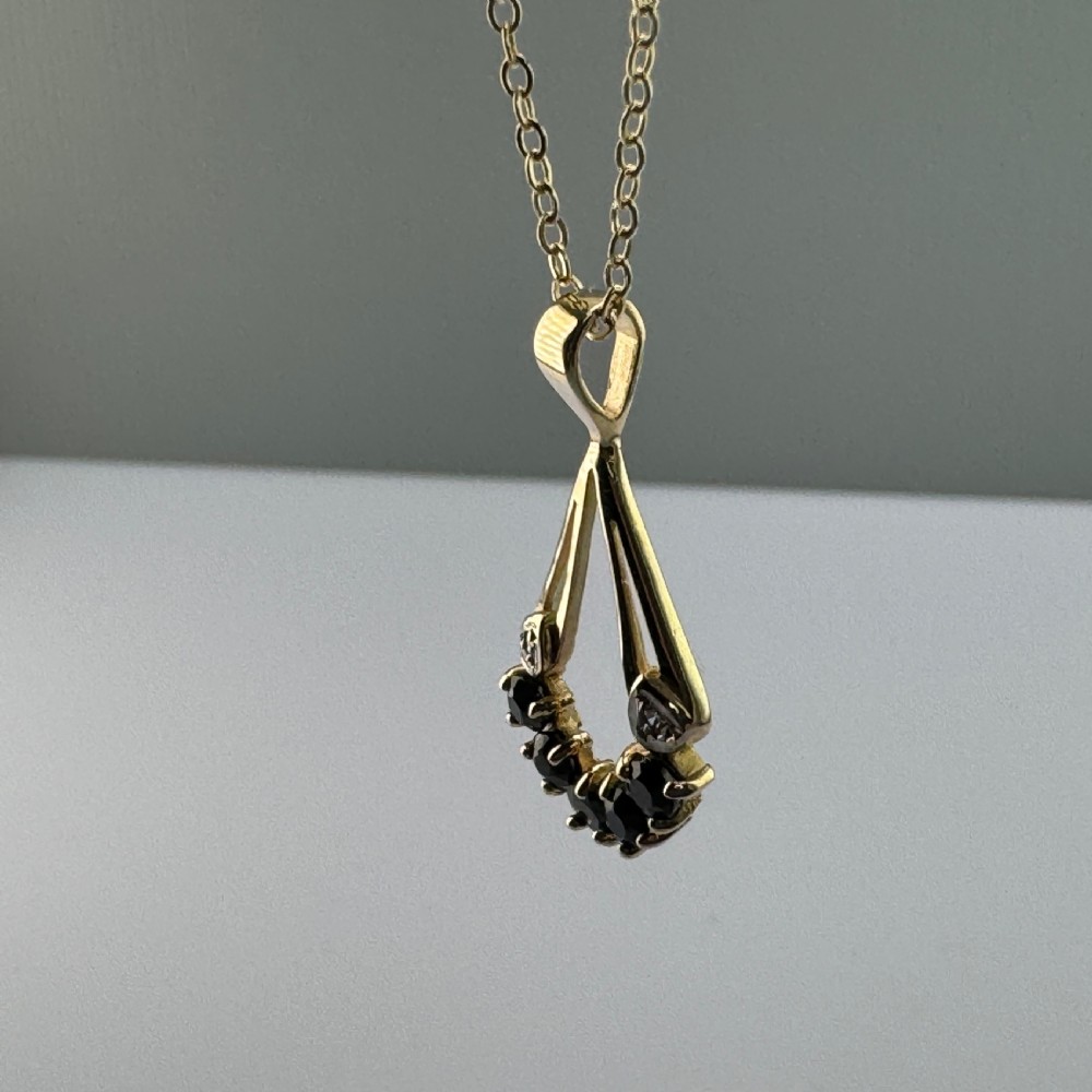 A 9ct yellow gold openwork drop pendant set with five round dark blue sapphires and two small accent diamonds on a fine chain. View IV
