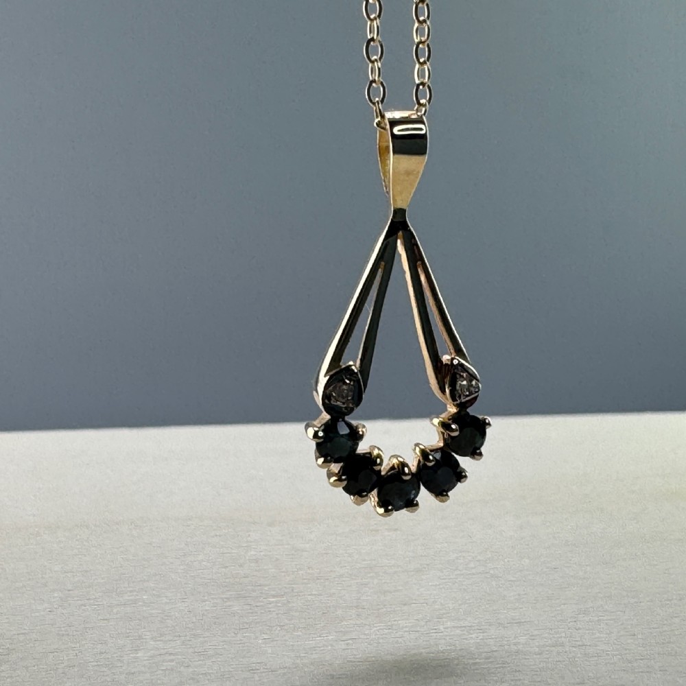 A 9ct yellow gold openwork drop pendant set with five round dark blue sapphires and two small accent diamonds on a fine chain. View VII
