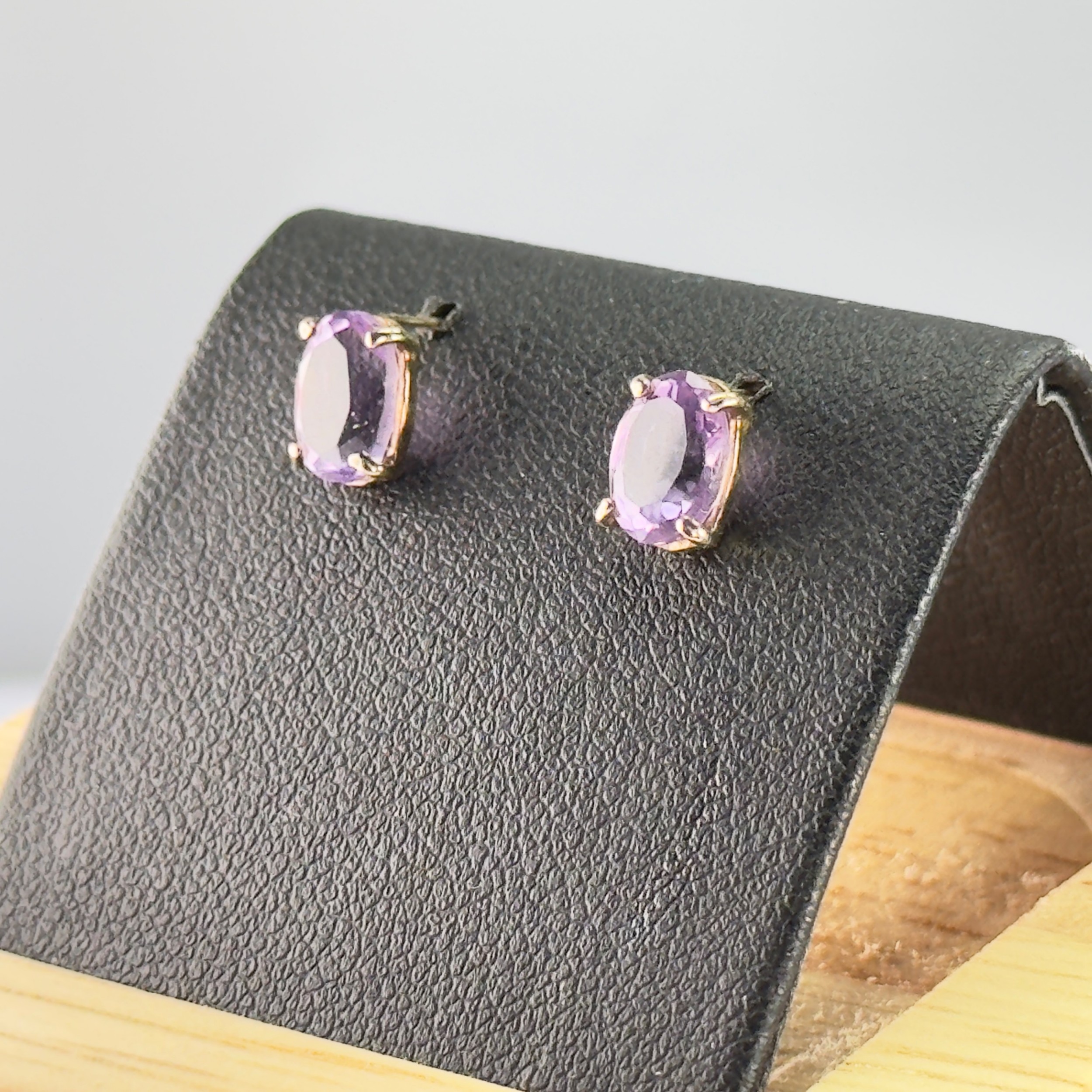 A pair of 9ct yellow gold stud earrings, each featuring an oval-cut purple amethyst gemstone in a four-claw setting.