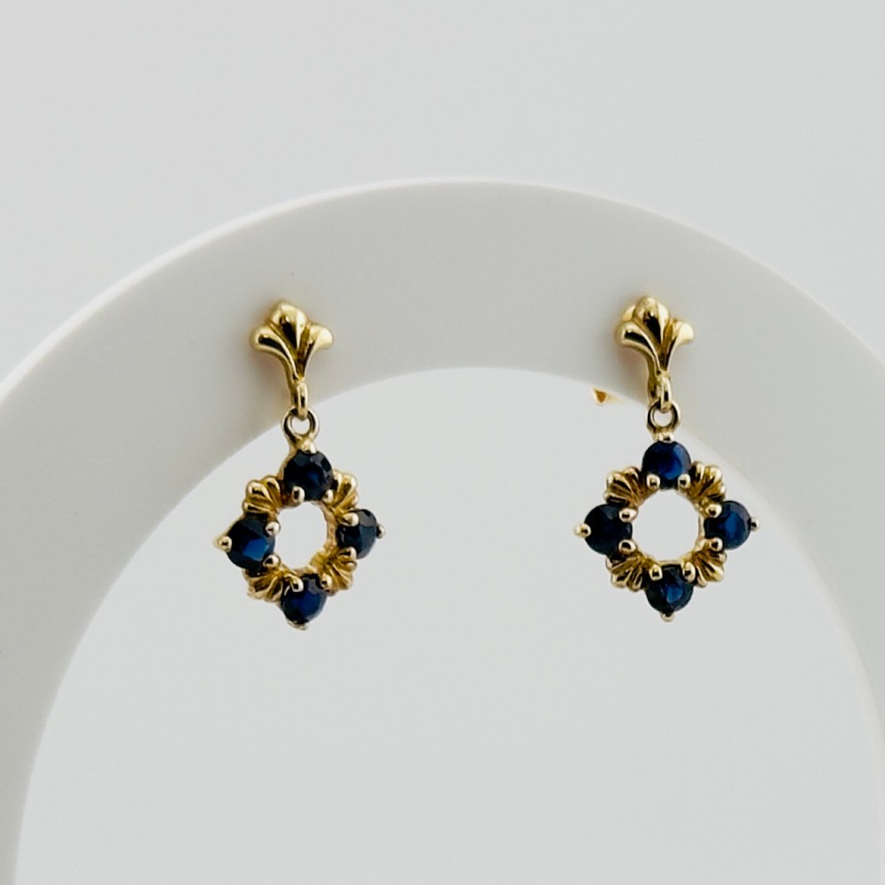 A pair of 9ct yellow gold drop earrings, each featuring a stud top with a suspended open circular pendant set with four dark blue sapphires.
