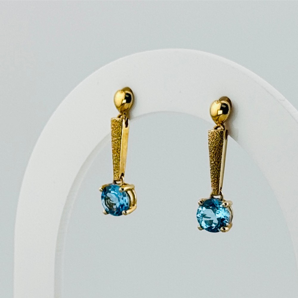 A pair of yellow gold drop earrings featuring textured tapering bars suspending round-cut blue zircon gemstones in four-claw settings.