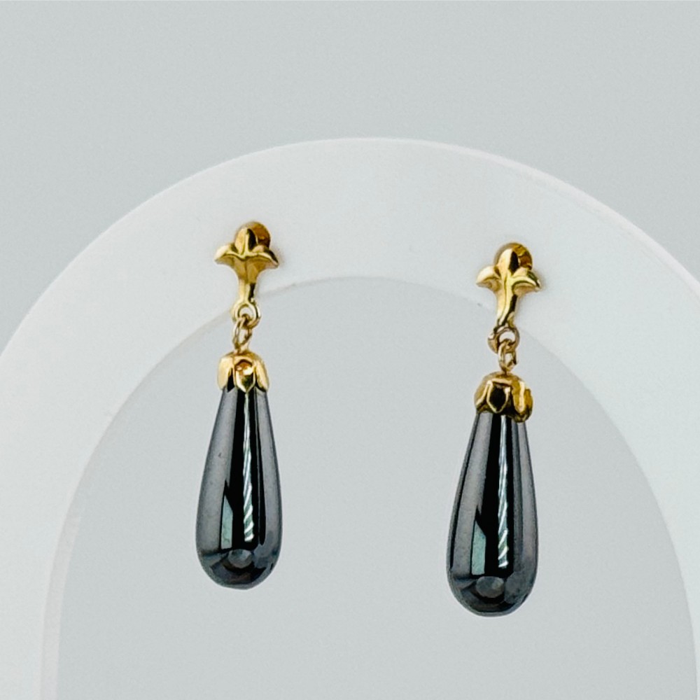 A pair of 9ct yellow gold drop earrings featuring metallic grey hematite teardrops suspended from stylised motif studs.