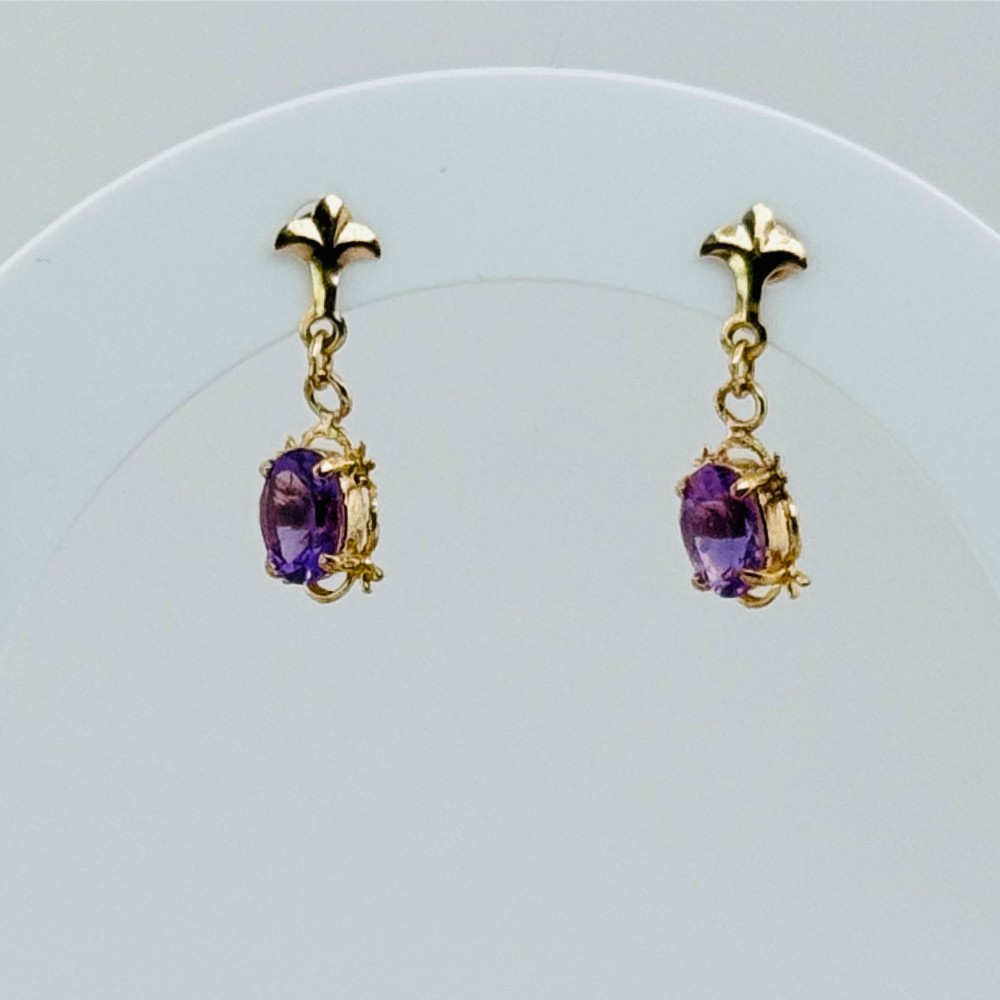 A pair of 9ct yellow gold drop earrings featuring fleur-de-lis stud tops suspending oval cut purple amethyst gemstones in claw settings.