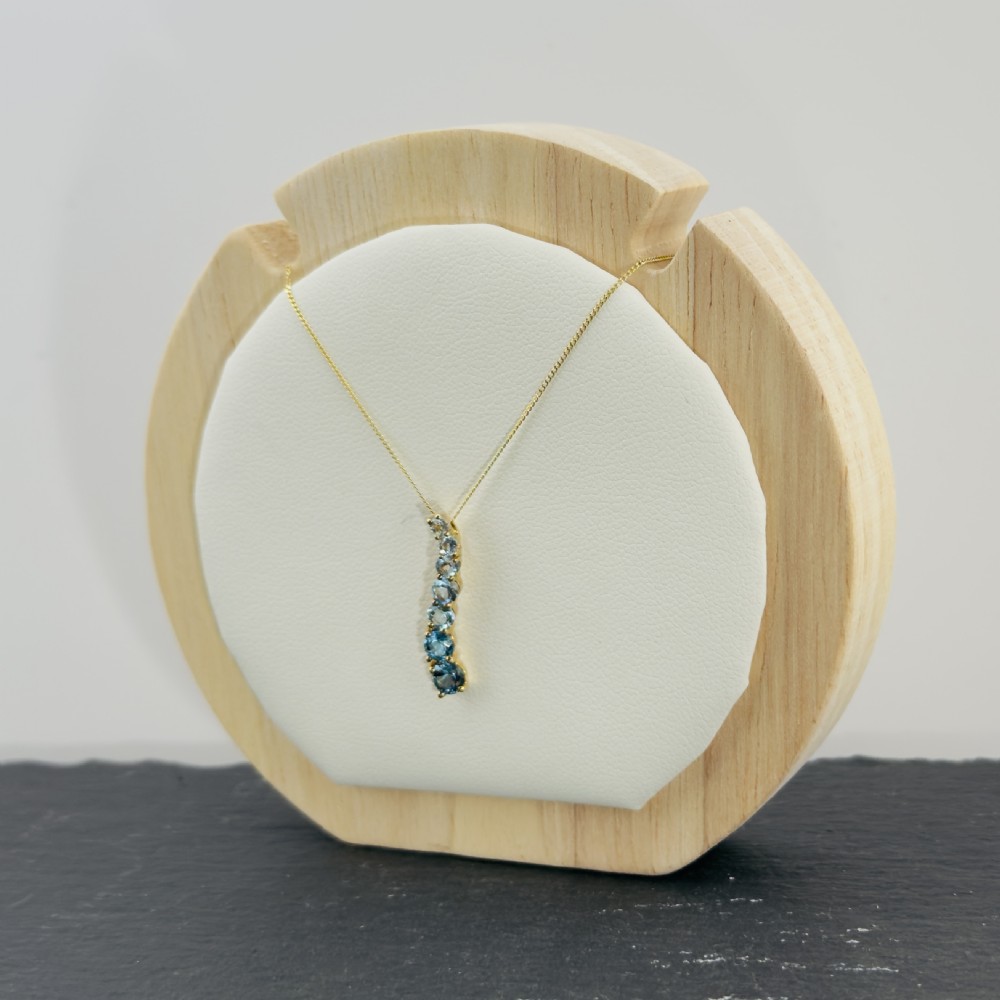 A 9ct yellow gold wave-shaped pendant featuring a vertical line of graduated blue topaz gemstones suspended from a fine chain. View III