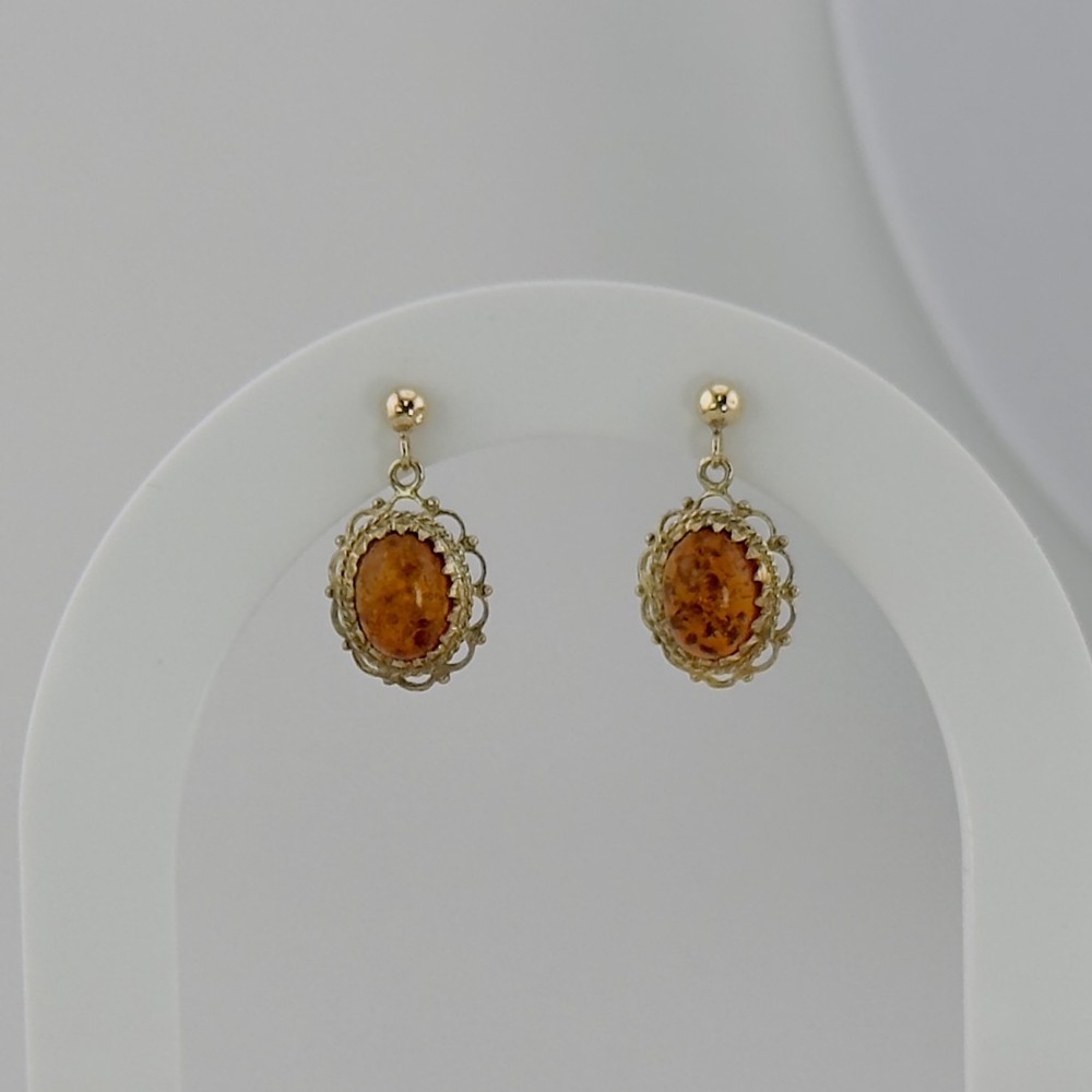 A pair of nine-carat gold drop stud earrings featuring oval amber stones set within ornate filigree borders.
