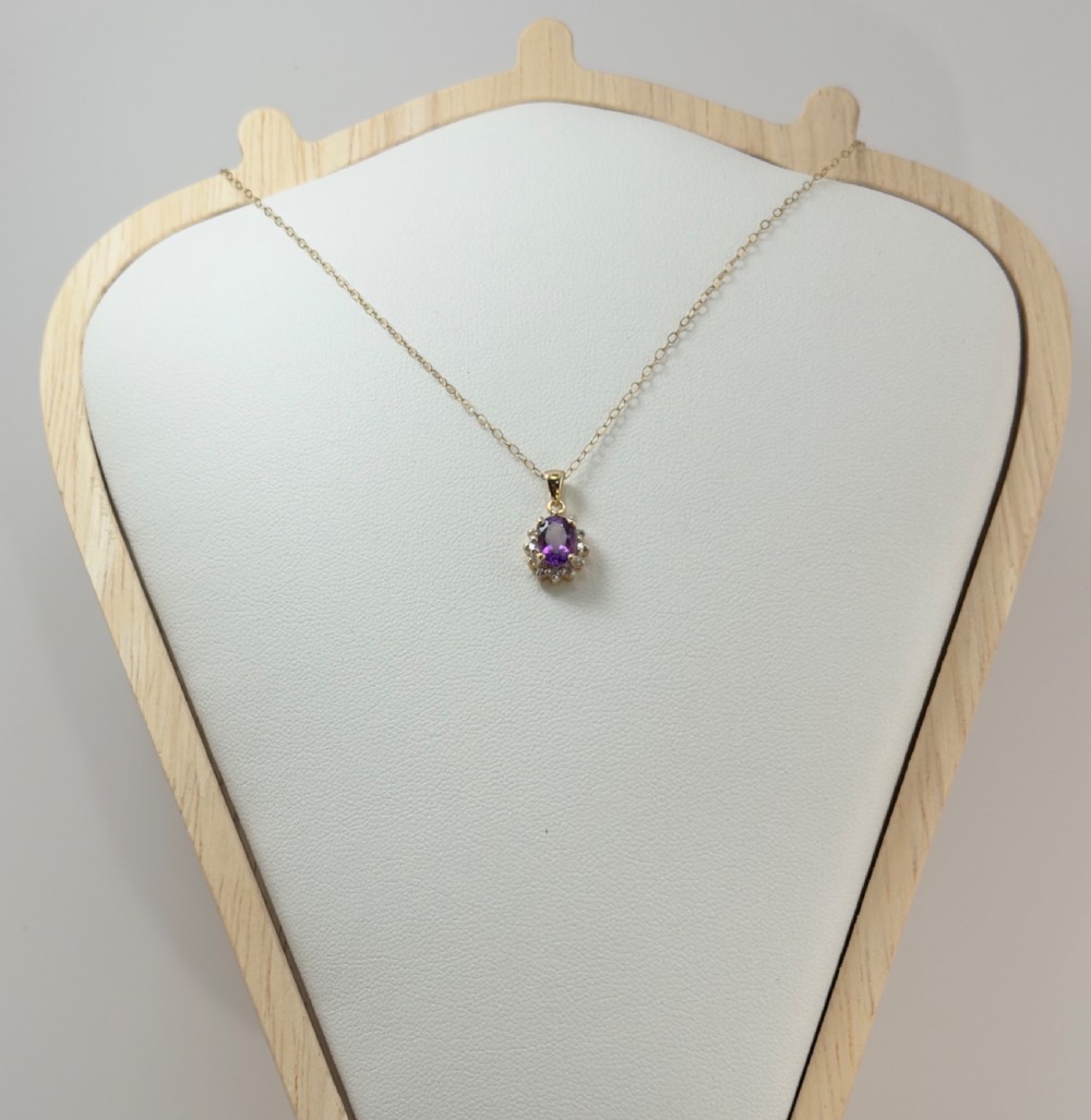 A 9ct yellow gold chain supporting an oval purple amethyst pendant surrounded by a cluster halo of small diamonds. View III
