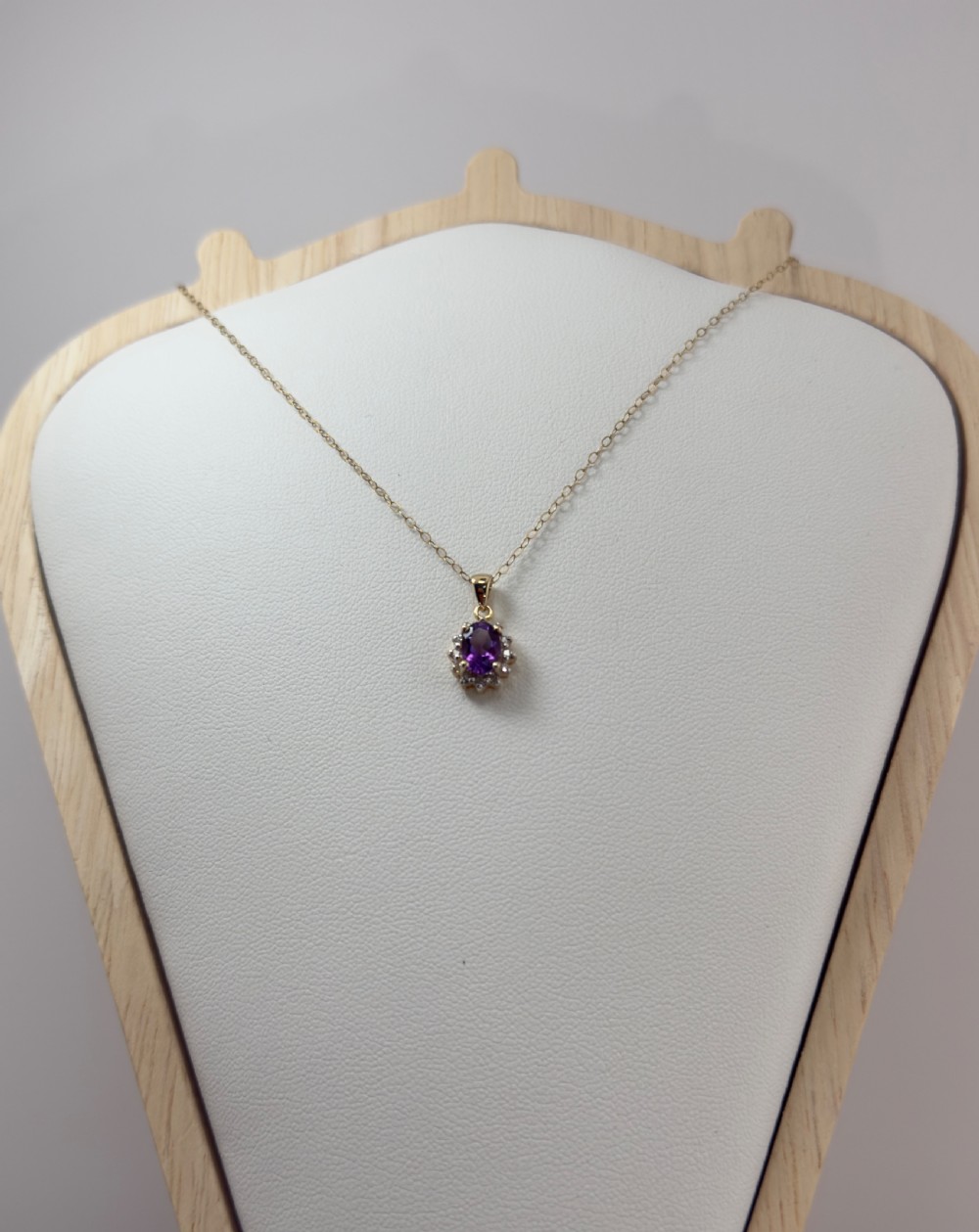 A 9ct yellow gold chain supporting an oval purple amethyst pendant surrounded by a cluster halo of small diamonds. View II