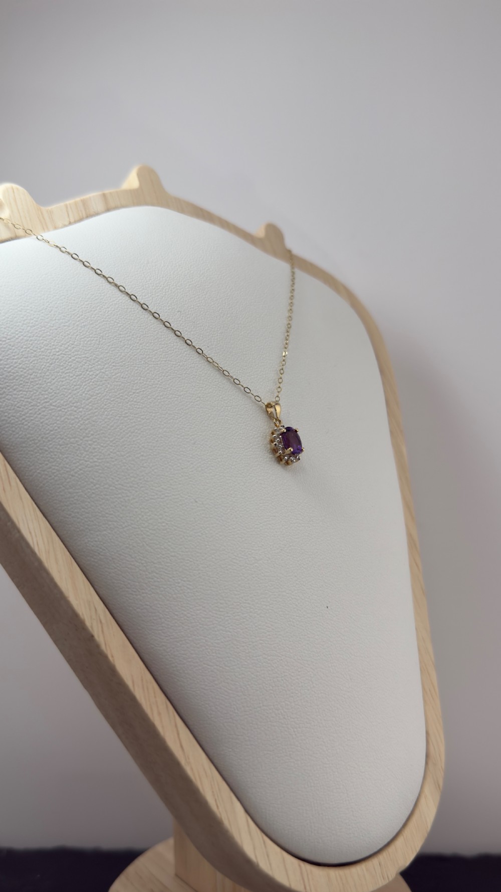 A 9ct yellow gold chain supporting an oval purple amethyst pendant surrounded by a cluster halo of small diamonds. View V