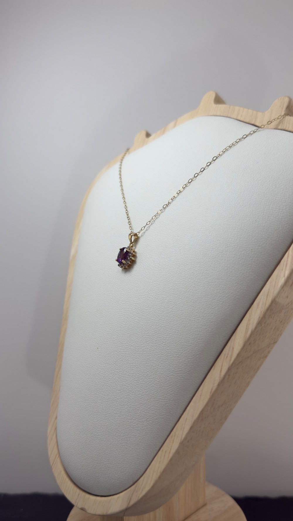 A 9ct yellow gold chain supporting an oval purple amethyst pendant surrounded by a cluster halo of small diamonds. View VI