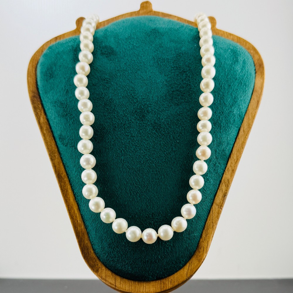 A single strand of round cream cultured pearls featuring a 14ct gold clasp displayed on a green velvet bust.