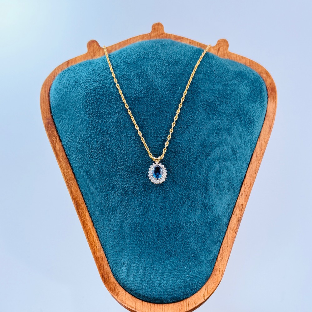 A 9ct yellow gold chain supporting an oval blue zircon pendant surrounded by a halo of small diamonds. View VI