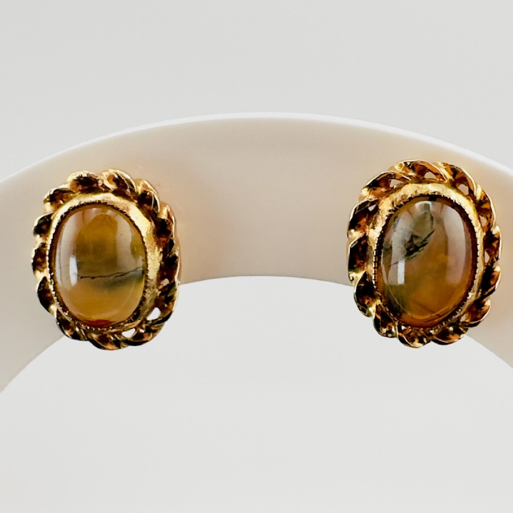 A pair of oval gold stud earrings with cabochon tigers eye gemstones framed by a twisted rope border.
