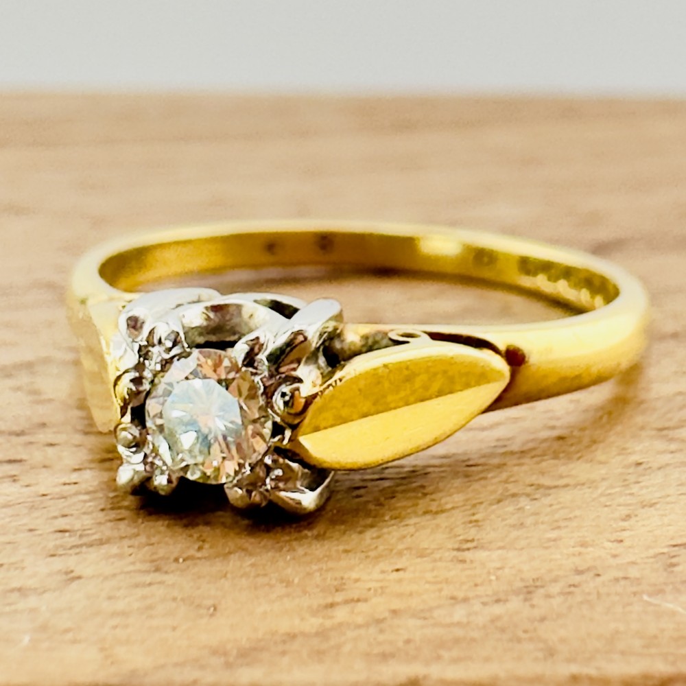 A Victorian 18ct yellow gold solitaire ring featuring a central round diamond set in an ornate illusion head with leaf shoulder accents.