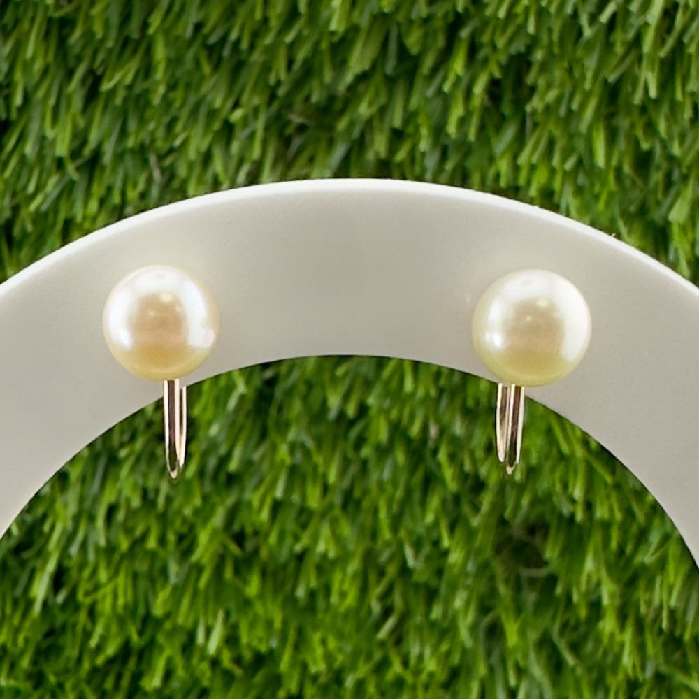 A pair of round cream pearl clip-on studs featuring 9ct yellow gold screw-back mechanisms.